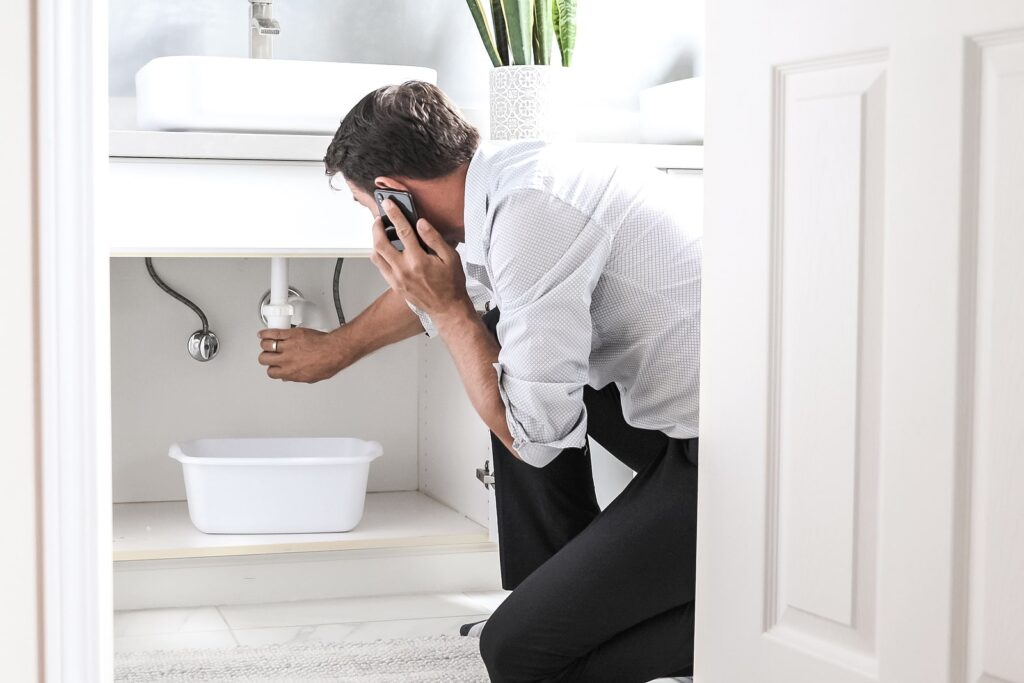 bigstock-Man-Calling-Plumber-In-Front-O-361105207-min